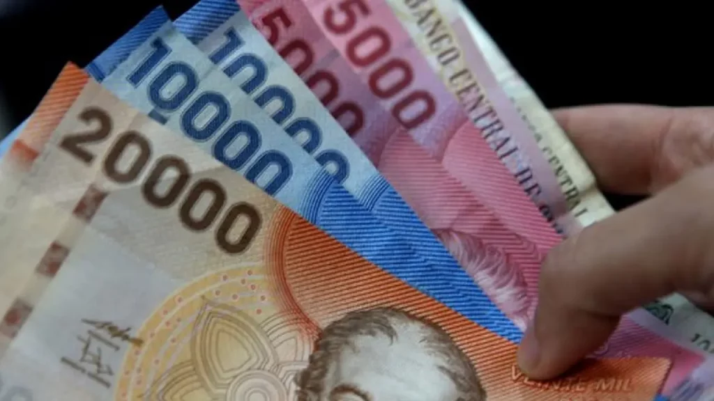 Notas de pesos chilenos em diferentes valores sendo seguradas por uma mão, indicando a importância de levar dinheiro em espécie para o Atacama.