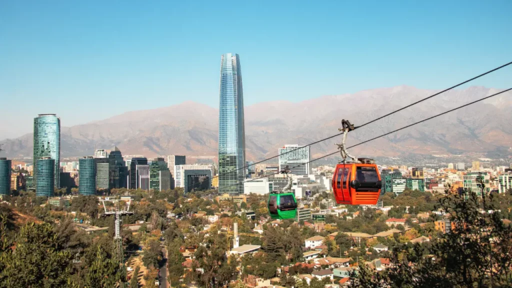Vista panorâmica de Santiago com o teleférico do Parque Metropolitano em destaque e a Cordilheira dos Andes ao fundo.