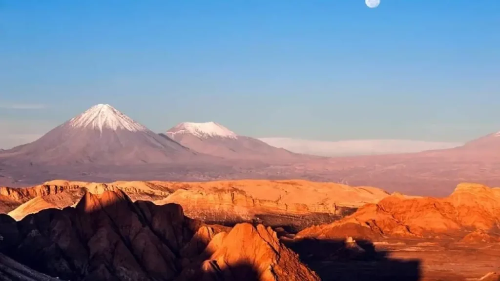 Fim de tarde no Valle de la Luna, no Deserto do Atacama, com céu alaranjado, formações rochosas e luz dourada refletindo na paisagem.