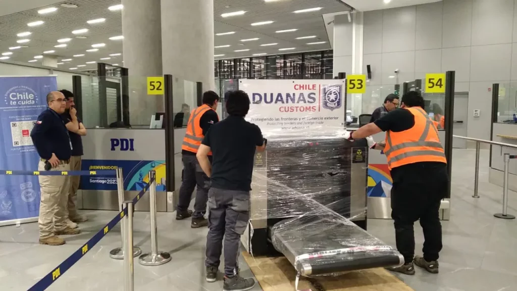 Funcionários da alfândega chilena inspecionam bagagens na área de desembarque do aeroporto de Santiago durante controle de entrada.