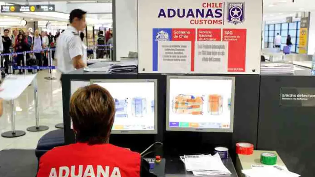 Agente da aduana chilena monitora bagagens no raio-x em aeroporto, verificando itens proibidos na entrada do país.
