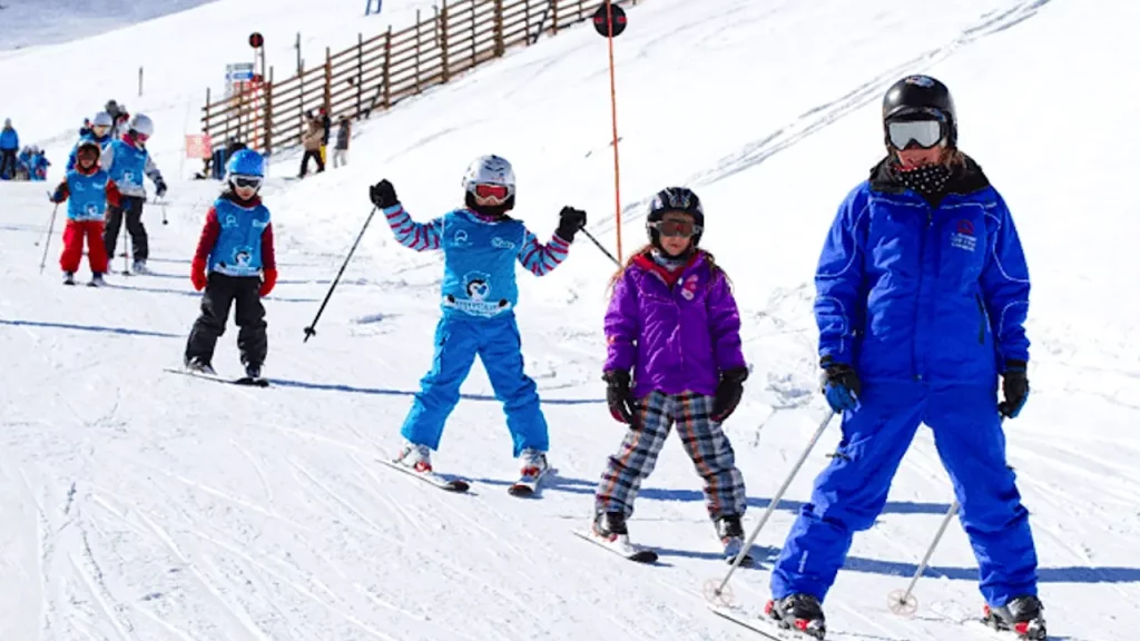 Um instrutor de esqui ensina um grupo de crianças pequenas em uma pista de neve para iniciantes.