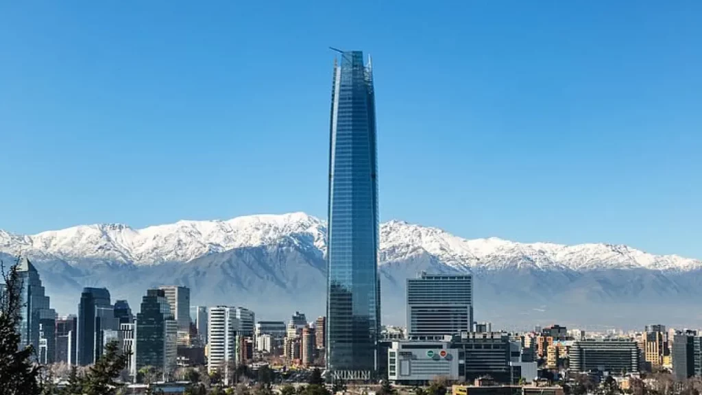 Torre Sky Costanera dominando o horizonte de Santiago com a Cordilheira dos Andes coberta de neve ao fundo, em um dia de céu limpo.