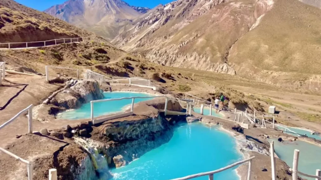 Piscinas naturais de águas termais em meio às montanhas no Cajón del Maipo, com águas azul-turquesa e trilhas ao redor.