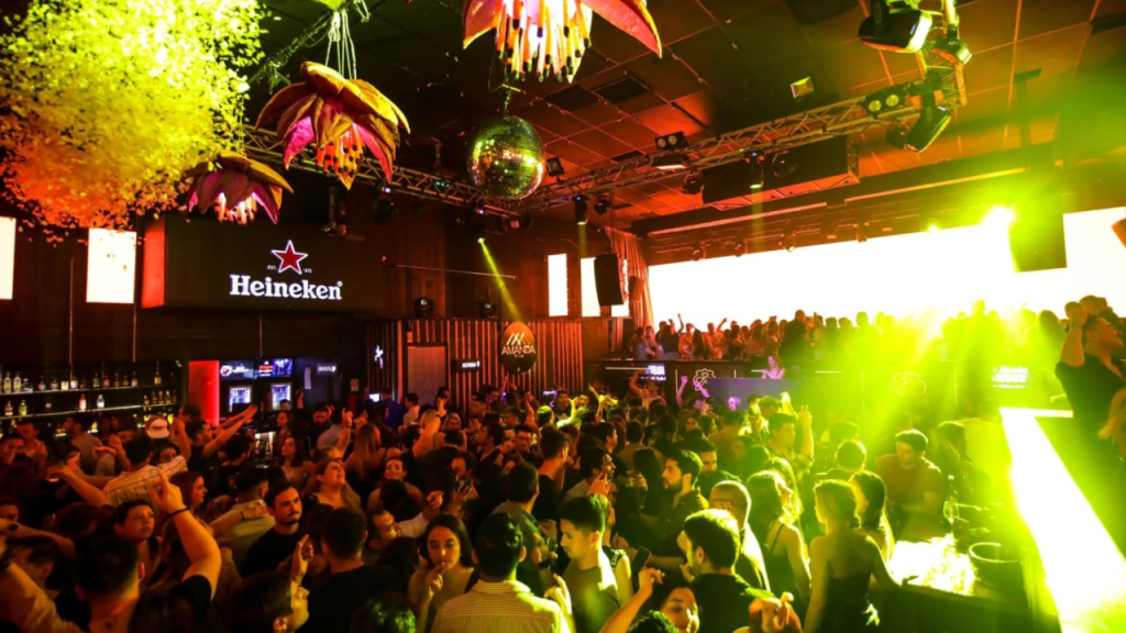 Pista de dança cheia no Club Amanda em Santiago, com iluminação intensa e decoração colorida durante a noite.