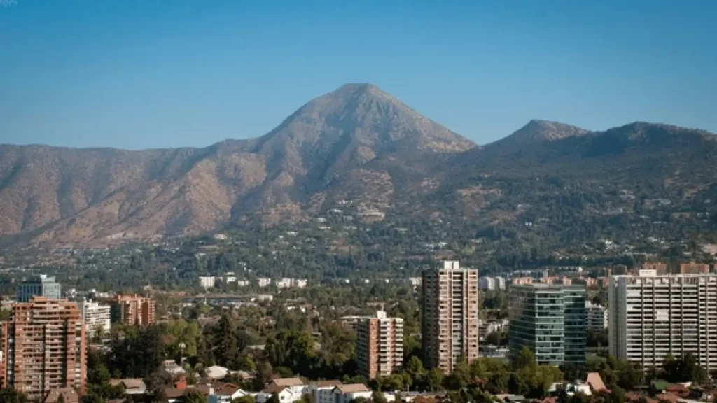 Vista panorâmica de Santiago com edifícios residenciais em primeiro plano e o Cerro Manquehue ao fundo, sob céu limpo.