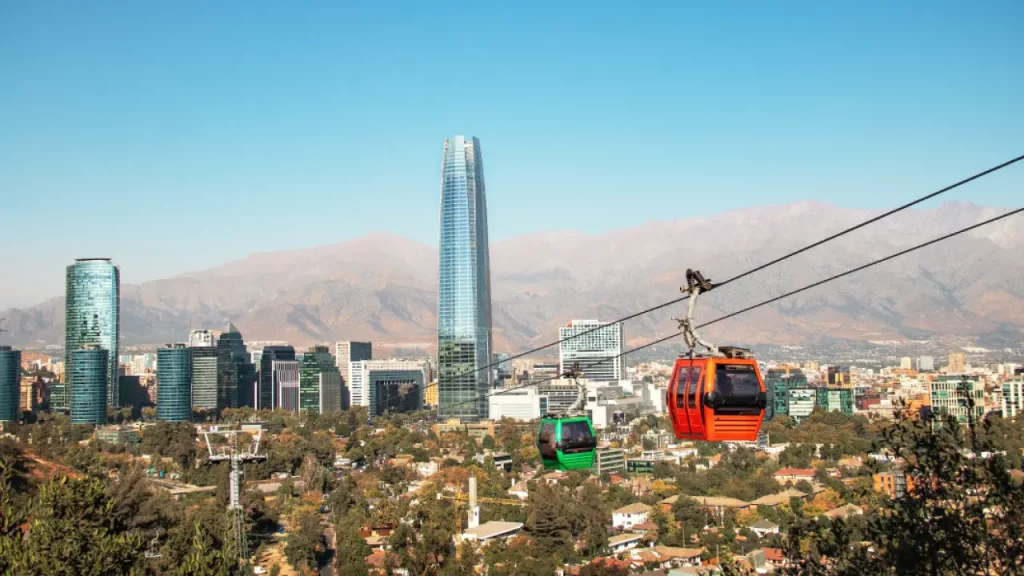 Teleférico passando sobre Santiago com o edifício Costanera Center ao fundo e a Cordilheira dos Andes ao horizonte.