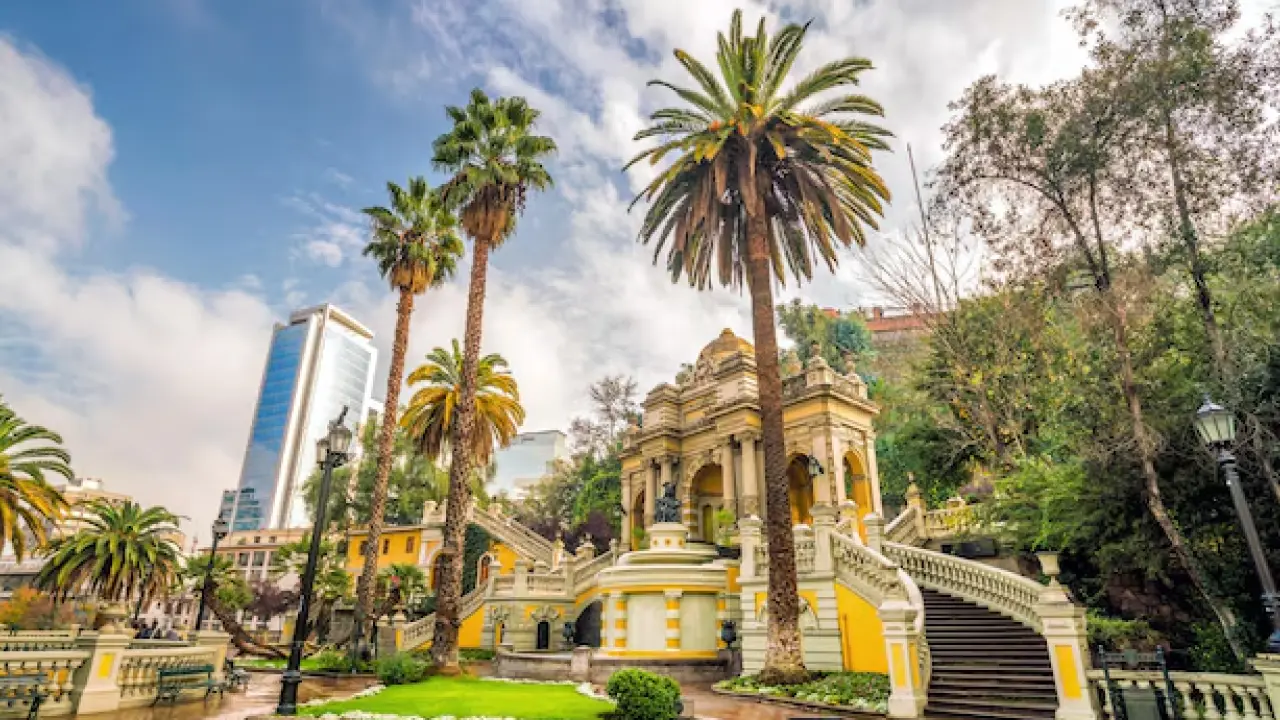 Escadarias históricas e palmeiras no Cerro Santa Lucía, em Santiago, com arquitetura clássica e prédios modernos ao fundo.