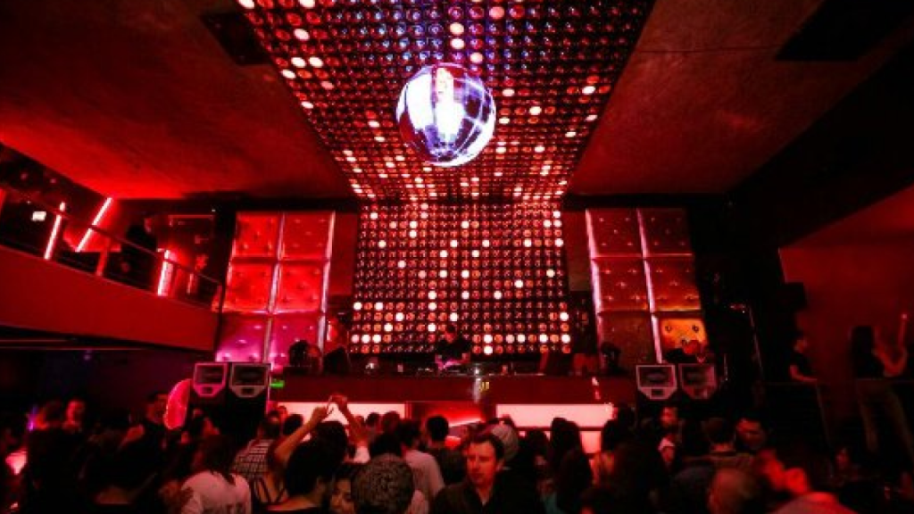 Interior da balada La Feria em Santiago, com globo espelhado no teto, iluminação vermelha e público curtindo música eletrônica.