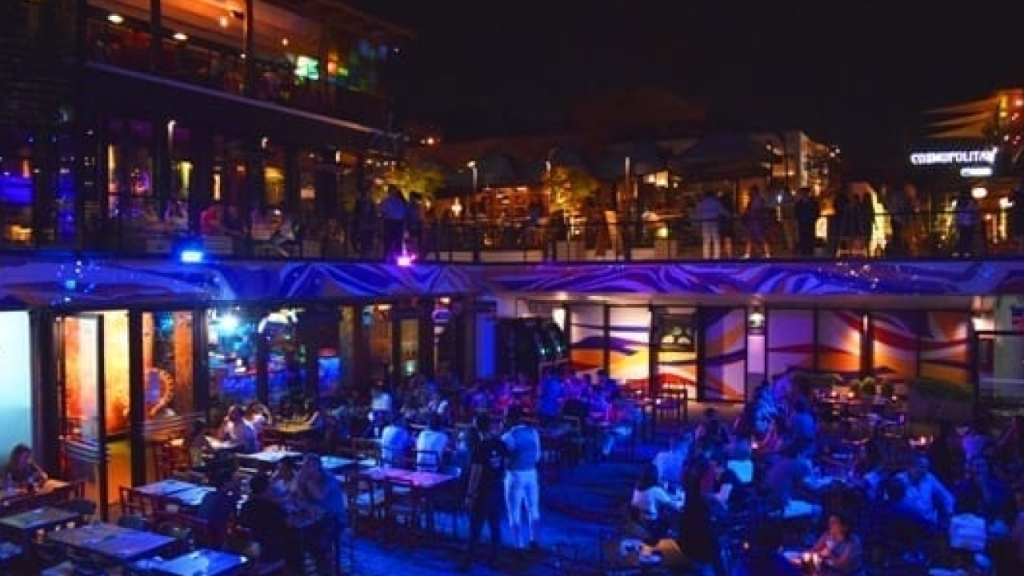 Terraço de bar com mesas ao ar livre e iluminação noturna em Santiago, Chile, com ambiente animado e pessoas conversando.