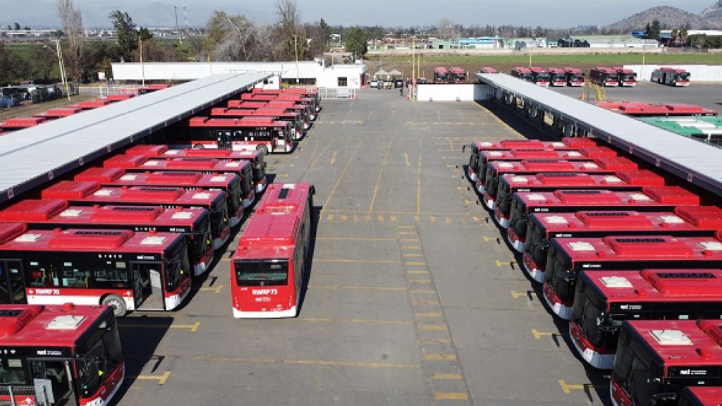 Estacionamento com dezenas de ônibus vermelhos do transporte público de Santiago organizados em fileiras.