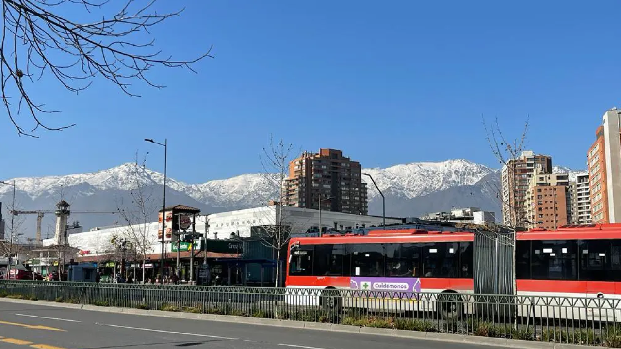 Ônibus do transporte público de Santiago circulando com a Cordilheira dos Andes nevada ao fundo, em um dia ensolarado.