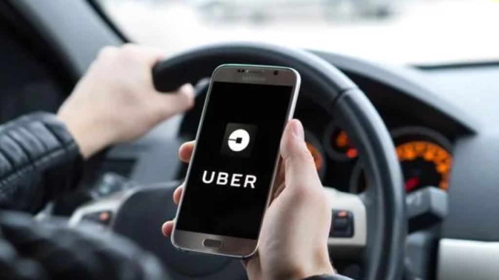Pessoa segurando celular com o aplicativo da Uber aberto, enquanto dirige um carro.