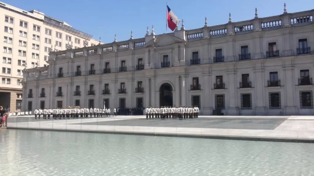 Cerimônia de troca da guarda em frente ao Palácio de La Moneda, com soldados alinhados e refletidos no espelho d'água da Plaza de la Ciudadanía.