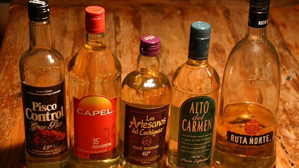Garrafas de pisco chileno alinhadas sobre mesa de madeira.