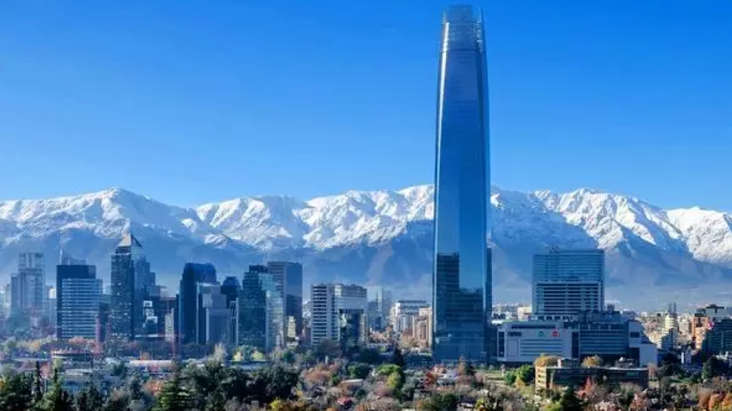 Skyline de Santiago com o Costanera Center e a Cordilheira dos Andes coberta de neve ao fundo em dia ensolarado.