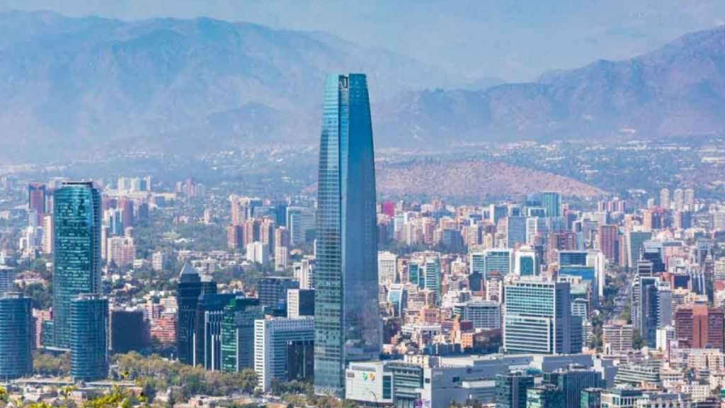 Vista panorâmica de Santiago do Chile com o Costanera Center em destaque, cercado por prédios e montanhas ao fundo.