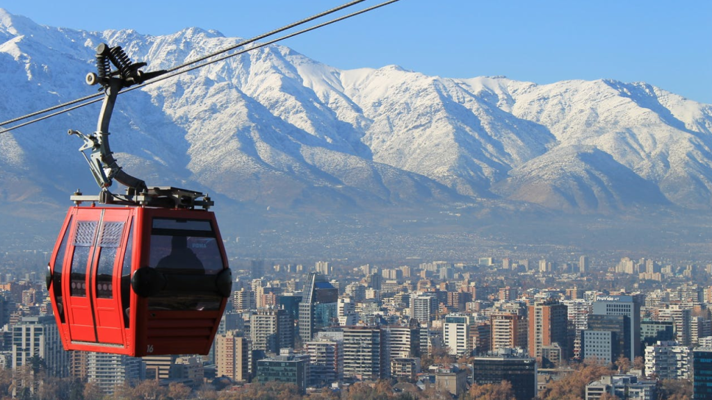 Cabine vermelha do teleférico de Santiago com vista para a cidade e a Cordilheira dos Andes coberta de neve ao fundo.