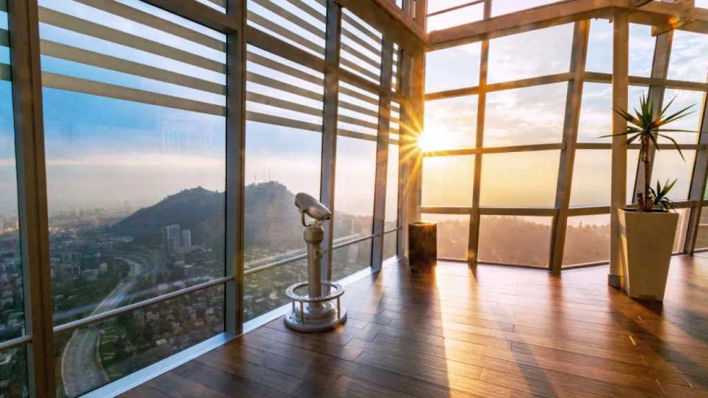 Vista do mirante Sky Costanera durante o amanhecer, com janelas envidraçadas, binóculo de observação e vista para o Cerro San Cristóbal.