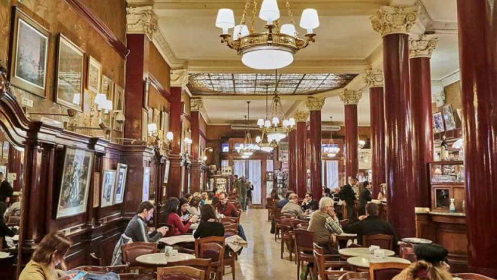 Interior de café histórico em Buenos Aires, colunas de madeira, luminárias antigas e mesas ocupadas.