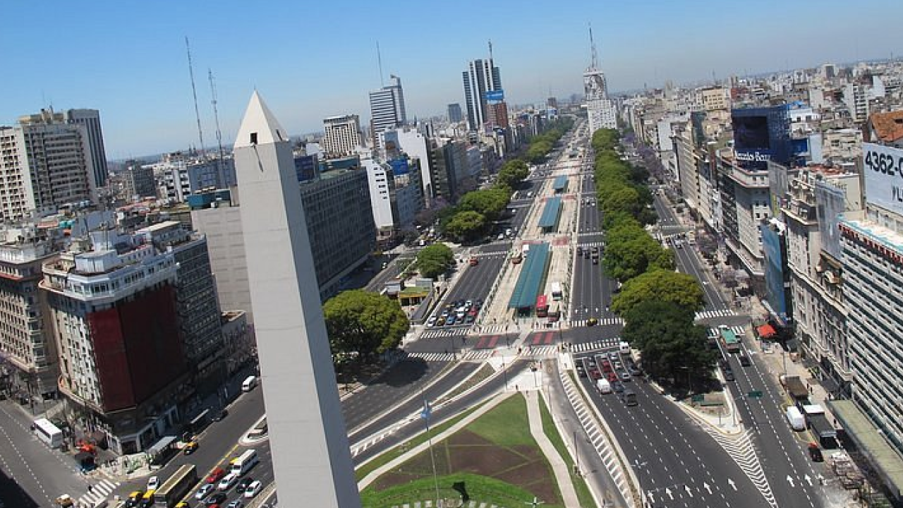 Vista elevada do Obelisco com a Avenida 9 de Julio ao fundo, canteiros centrais e tráfego intenso.