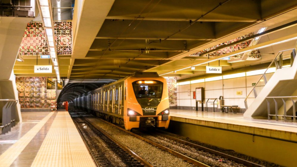 Trem do Subte chegando a uma estação moderna de Buenos Aires, plataforma iluminada e sinalização “Salida”.