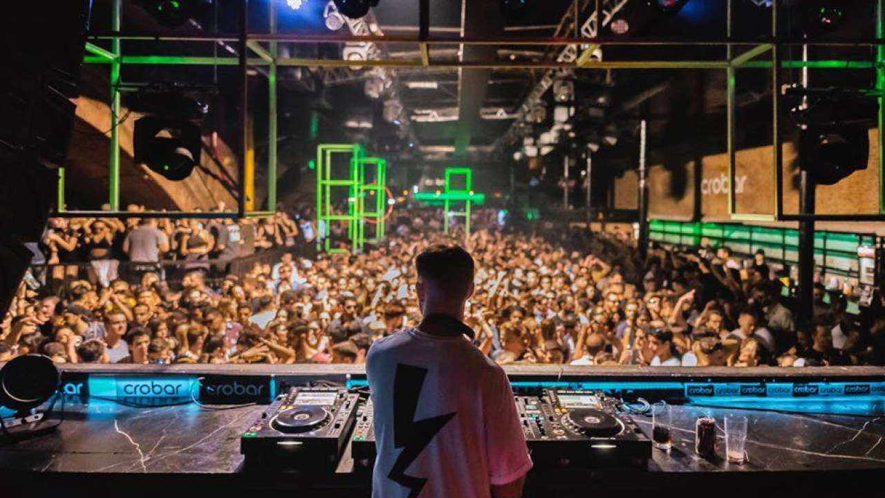 DJ visto de costas tocando no Crobar para multidão com estruturas luminosas verdes.